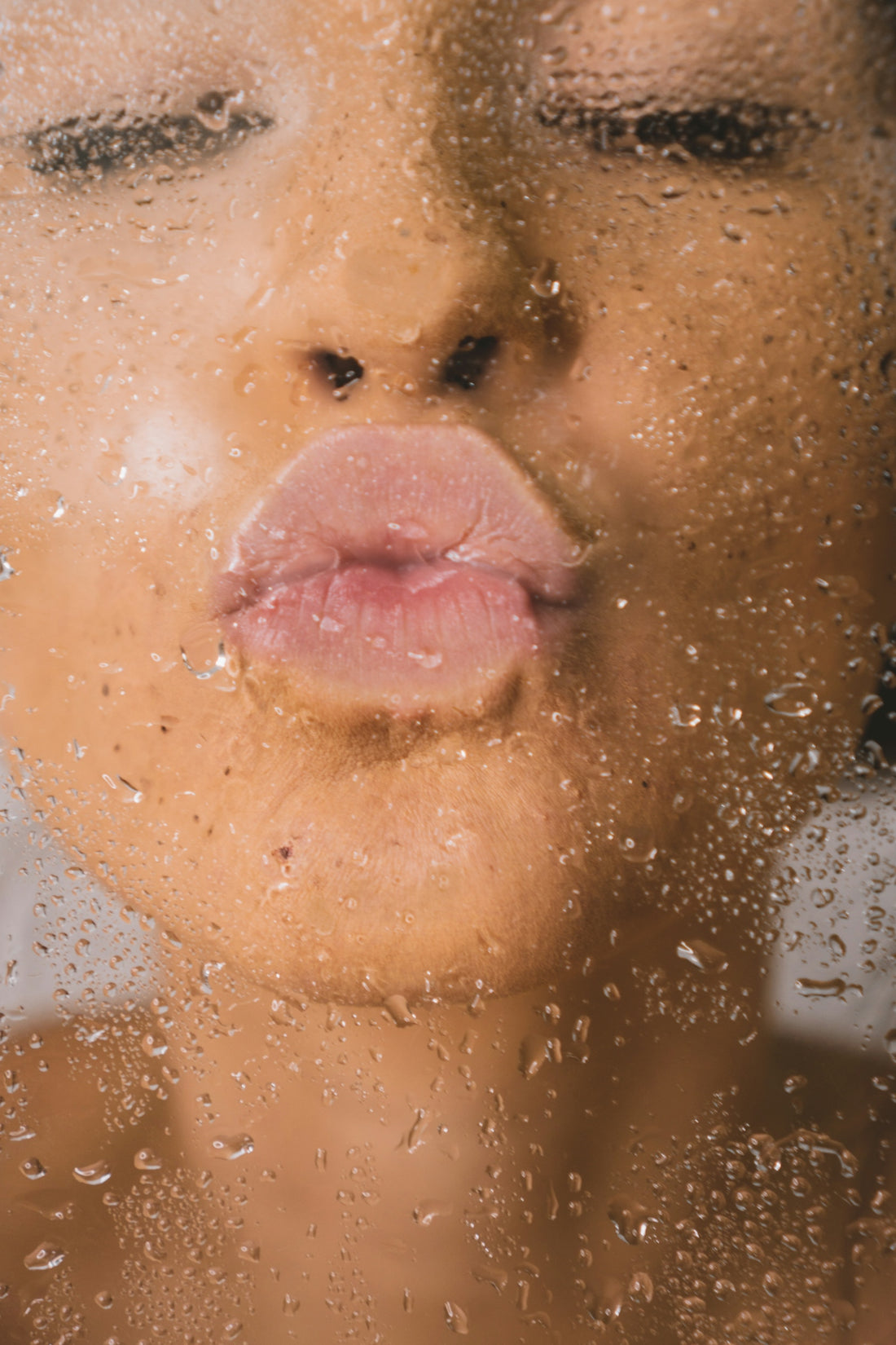 A person pressing their lips against a glass surface covered in water droplets
