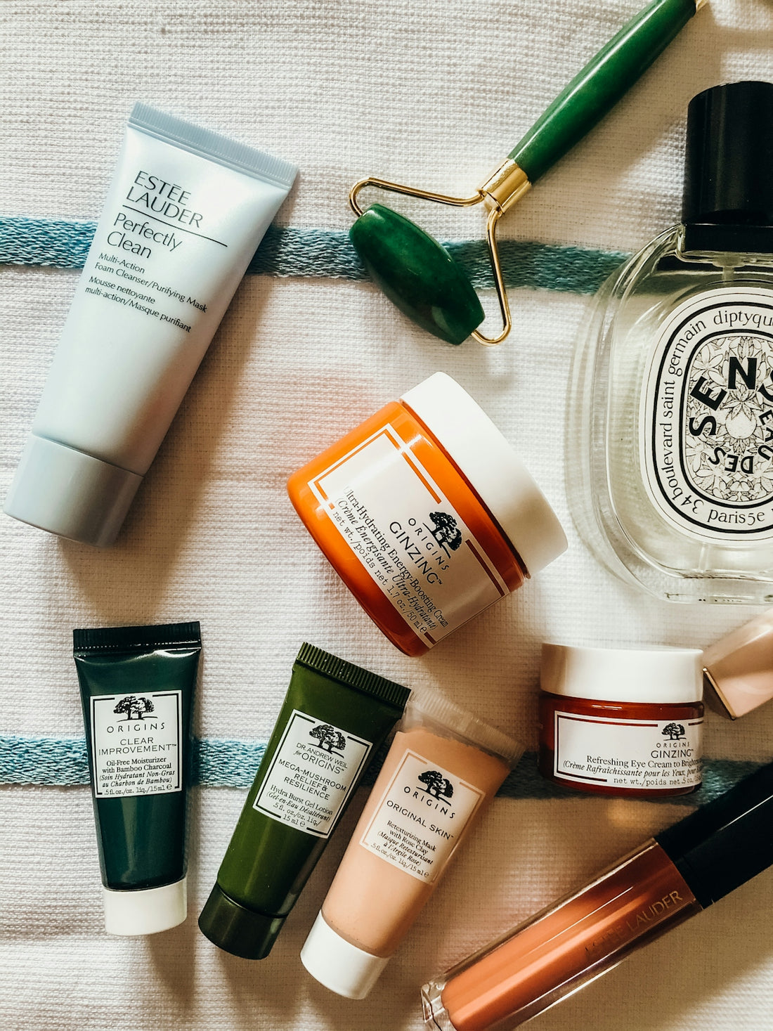 Assorted skincare products and a green jade roller on a white striped towel