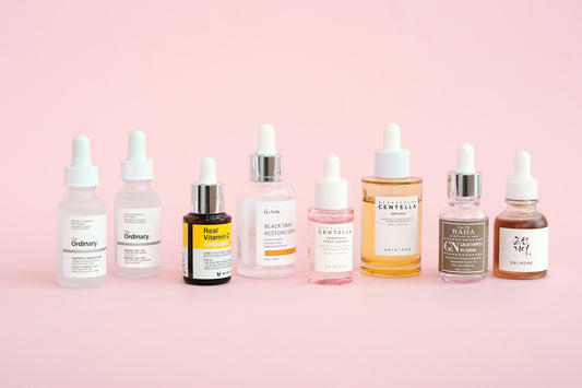 Skincare bottles are displayed on a pastel pink background.